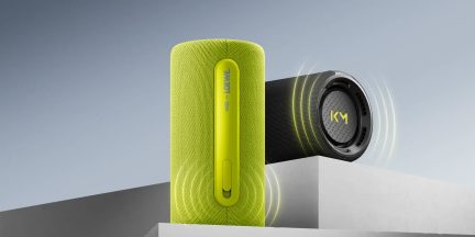 Prenosni Bluetooth zvočnik v zeleni in črni barvi s tekstilno mrežico, valjaste oblike in vidnimi stranskimi gumbi