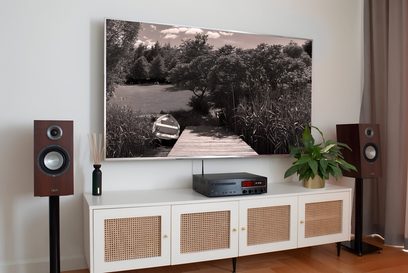 Wit TV-meubel met geïntegreerd Taga Harmony HTR-1500CD zwart hifi-systeem, luidsprekers, versterker, cd-speler, onder een televisie die een boslandschap toont