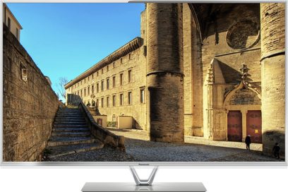 Panasonic TX-L50DT60E tv-skærm, der viser en brolagt gade omgivet af gamle stenbygninger