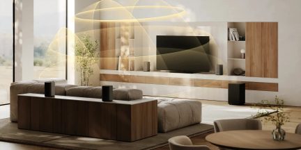 Sistem home cinema cu patru boxe wireless negre în jurul unui living modern cu televizor montat pe perete