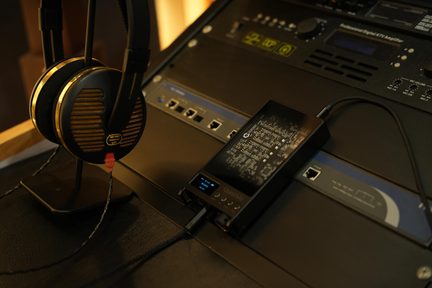 Aranyszínű Sennheiser HD 540 hifi fejhallgató állványon, hordozható Questyle audio DAC-hoz csatlakoztatva stúdiókonzolon