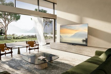 Moderní obývací pokoj s velkou televizí, zelenou pohovkou, skleněným konferenčním stolkem, 2 dřevěnými křesly a francouzským oknem s výhledem do zahrady