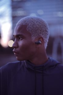 Billedet viser profilen af en sort mand med kort og krøllet hår, der bærer en sort trådløs øretelefon i øret