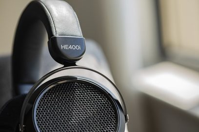 Hifiman HE400i 2020 izdevuma atvērtā tipa hifi austiņas, skatītas no kreisās puses, ar melnu režģotu skaļruni, pelēku loku un spilventiņiem