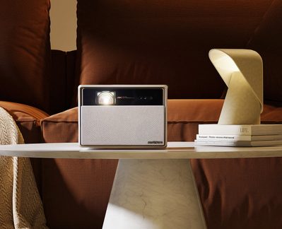 4K-projektor på hvid hylde mellem gylden lampe og bøger i rum med brune vægge og gardiner