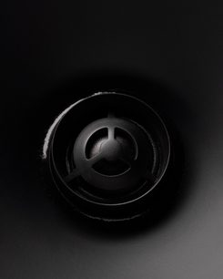 Zwarte ronde luidspreker in close-up, centrale geperforeerde grill met drie radiale steunen, omliggend oppervlak glad