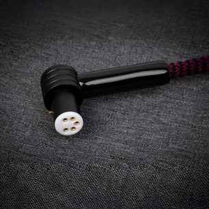 Nærbilde i skrå vinkel av den blanke, svarte vinklet DIN-kontakten med hvitt innstikk og fem forgylte pinner, koblet til en svart og magentafarget flettet tekstilstrømpe på Thorens PhonoConnect PHC 150 DIN-RCA 1,5 m phono-kabel