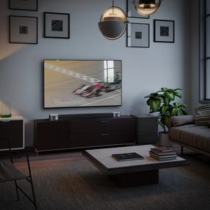 Fladskærms-tv, der viser et billøb i en moderne stue med sofa, sofabord, planter og rammer på væggen
