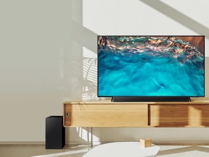 Fladskærms-tv, der viser et turkisfarvet undervandsscene på et lyst trækabinet med en sort Samsung HW-B450/ZF soundbar