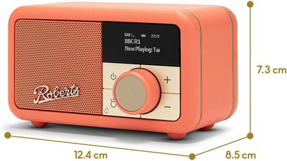 Rádio Roberts Revival Petite 2 v oranžové barvě, kompaktní obdélníkový kryt potažený zrnitou umělou kůží, pohled z pravého předního tříčtvrtečního úhlu, přední strana s perforovanou mřížkou a logem vlevo, malý černý displej a béžový panel s velkým kruhovým tlačítkem a ovládacími tlačítky vpravo