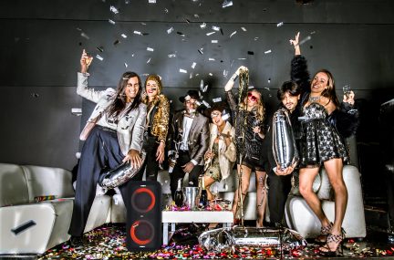 Billedet viser en gruppe af smilende og entusiastiske unge kvinder, der fejrer under en regn af sølvfarvede konfettier, iført festlige og glinsende outfits