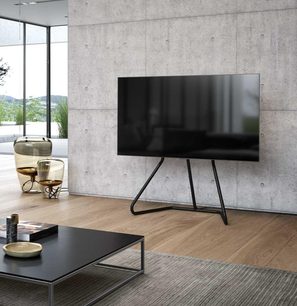 Sort TV-møbel på metalben, fladskærm, i en moderne stue med glasparti og lyst trægulv