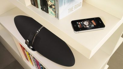 Must Bowers & Wilkinsi Zeppelin Air kõlar valge riiulil, peal iPhone, millel kuvatakse albumi kaanepilt