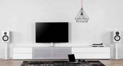 Meuble TV blanc laqué avec tiroirs, étagères et emplacement central pour écran plat, deux enceintes blanches, lampe noire suspendue