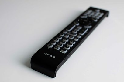 Télécommande iR14 Cyrus, vue en perspective, surface noire, boutons gris, logo visible, fond blanc, angle incliné