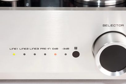 Frente prateada em alumínio escovado do amplificador integrado estéreo valvulado Cayin CS-300A preto, vista frontal em close, com seis LEDs multicoloridos alinhados sob serigrafias e um grande botão circular de seleção à direita