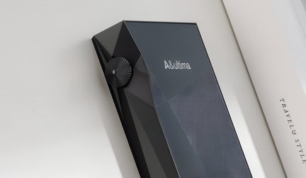 Stačiakampis juodas įrenginys su tekstūruotu paviršiumi, šoniniu apvaliu ratukiniu mygtuku ir baltu logotipu viršuje