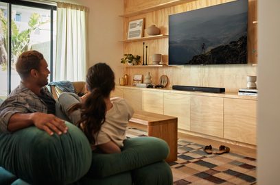 Stue med grøn sofa, par sidder og ser på vægmonteret TV, lyst træmøbel til TV med sort soundbar
