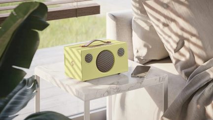 Diffusore portatile verde chiaro con tre griglie circolari e maniglia sulla parte superiore, appoggiato su un tavolino d’appoggio
