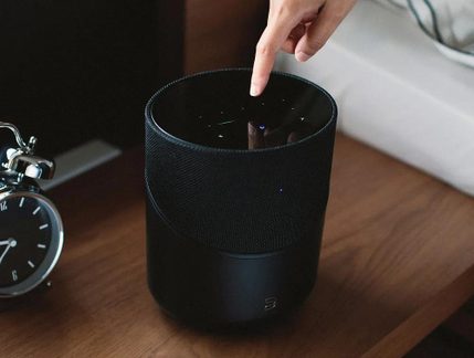 Sort cylinderformet højttaler i stof og plast, blank LED-berøringsfølsom top, berørt med finger, set ovenfra
