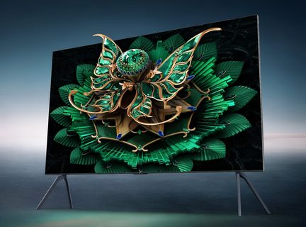 Schwarzer Flachbildfernseher mit dünnem Metallrahmen auf zwei schrägen Standfüßen, aus vorderer linker Dreiviertelansicht, Bildschirm zeigt eine grün-goldene 3D-Illustration