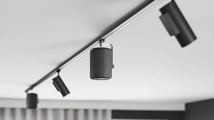 Musta sylinterimäinen kaiutin ripustettuna kattokiskoon useiden mustien suunnattavien kohdevalaisimien väliin