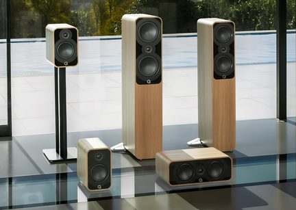 Set aus fünf Hi-Fi-Lautsprechern mit hellem Holzfurnier, rechteckigen Gehäusen mit abgerundeten Ecken und schwarzen Frontseiten, jeweils mit zwei grauen Woofern, zentralem Hochtöner und weißem Q-Logo, aus leicht schräger Frontalansicht