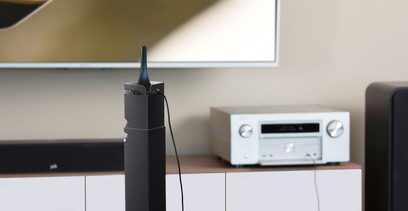 Denon AVC-X8500H sort hjemmebiograf-forstærker, delvis set forfra, med oprejst Wi-Fi-antenne, ved siden af et hvidt møbel