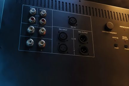 Painel traseiro de amplificador de áudio preto com entradas RCA e XLR, saída LFE e ajustes de frequência