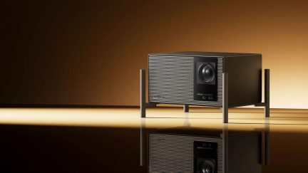 Videoproiettore Harman Kardon nero IMAX Enhanced, pannello frontale scanalato e obiettivo centrale, vista di tre quarti
