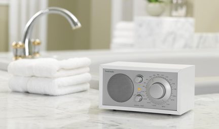Radio da tavolo bianca in plastica, griglia metallica, grande pulsante di regolazione, vista a tre quarti, su piano in marmo