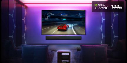 Frontalt udsyn til et videospilrum oplyst af lyserøde og lilla LED-lys, med et stort sort vægmonteret tv med glasoverflade, der viser et racerløbsspil, installeret over en sort, rektangulær soundbar, to mørkeblå stofsæder synlige i forgrunden
