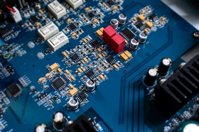 Blåt printplade med guld- og sølvfarvede elektroniske komponenter, røde kondensatorer, nærbillede set ovenfra