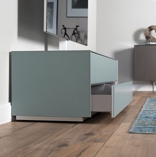 Lys grå mat TV-møbel med skuffer, på parketgulv, i et moderne minimalistisk interiør med blåt tæppe og dekorationer