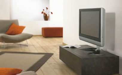 Sort TV-møbel, grå sofa, orange puder, hvid vase med røde blomster, fladskærm på grå vægbeslag