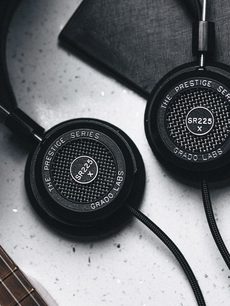 To åbne hovedtelefoner, Grado SR225x og Grado SR225, ligger på en grå, tekstureret overflade set ovenfra
