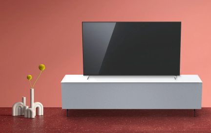 Bílý televizní nábytek, vypnutá černá televize, dva bílé vázy, dvě zelené rostliny, růžová stěna