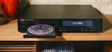 Schwarzer CD-Player NAD C 589 mit geöffneter CD-Schublade und Frontdisplay, Vorderansicht auf einem Holzmöbelstück
