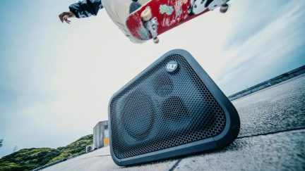 Svart Sony ULT Field bærbar høyttaler med perforert gitter, plassert i skateparken under en skateboarder i et hopp