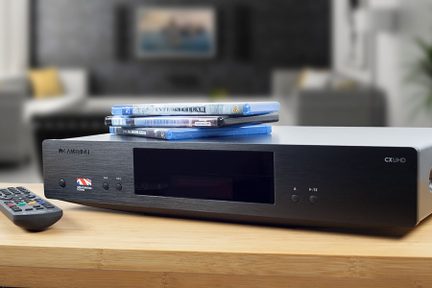 Lecteur Blu-ray noir posé sur une table en bois, avec des disques Blu-ray empilés à côté et une télécommande