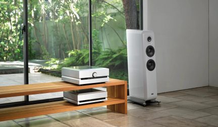White three-driver hi-fi floorstanding speaker, paired with two white audio components on a wooden cabinet