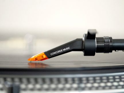 Juoda patefonų galvutė su auksinėmis raidėmis "CONCORDE MUSIC", padėta ant sidabrinės patefonų plokštelės
