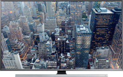 Samsung UE85JU7000-fjernsyn der viser et luftfoto af skyskrabere i en stor tætbefolket by ved skumringen
