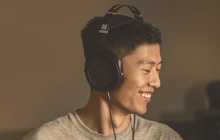 Black HiFiMan over-ear open-back headphones, worn in profile by a smiling man in a gray t-shirt
