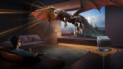 Salon întunecat, canapea gri, lampă de podea, proiector, ecran cu dragon zburător, persoană așezată cu ochelari 3D