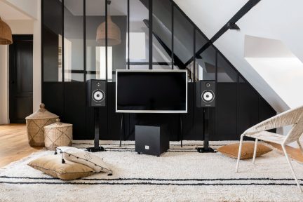 Black audio system with two vertical speakers, a subwoofer, and a central screen, placed on a rug in a modern living room