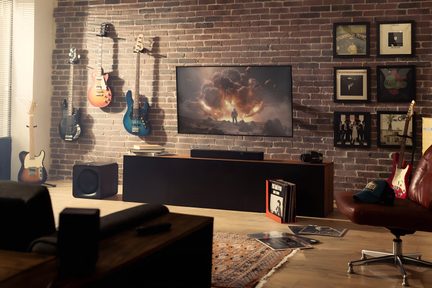 Loftový obývací prostor s velkoformátovou televizí, soundbarem, subwooferem, nástěnnými elektrickými kytarami a vinylovými deskami na podlaze