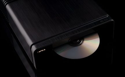 Black brushed-metal CD player, three-quarter front view, slot with partially inserted disc, illuminated logo on the left
