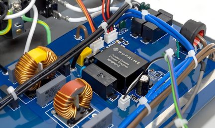 Vista ravvicinata di un circuito elettronico con componenti visibili: trasformatori, condensatori, cavi, connettori, scheda blu