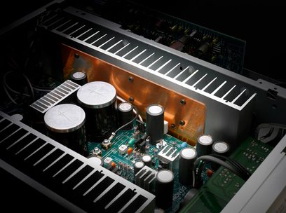 Indvendigt syn af en Denon PMA-1510AE hi-fi stereoforstærker, der viser elektroniske komponenter på et printplade og en varmesprederen i kobber